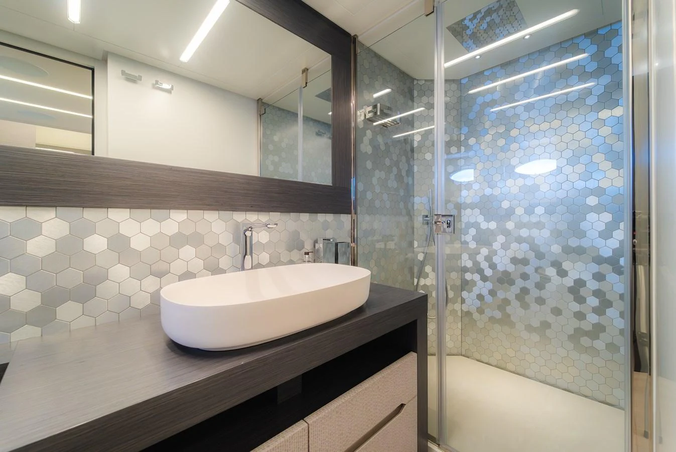 A modern yacht bathroom featuring a sleek sink and a glass-enclosed shower with hexagonal tiles. aboard NOVA Yacht for Sale