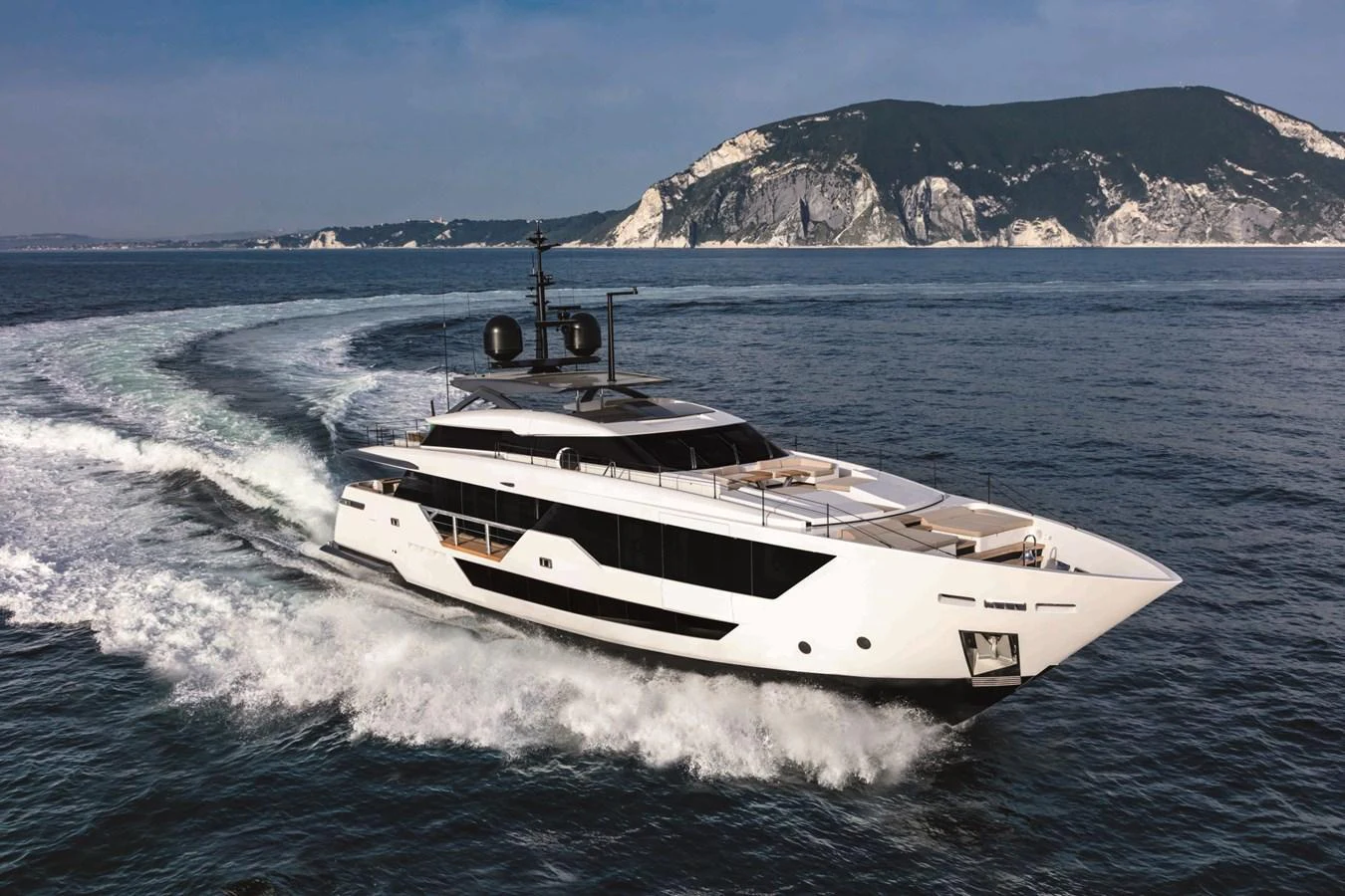 A sleek and modern yacht cruises through the open water with a scenic coastline in the background. aboard CUSTOM LINE SAETTA 128/02 Yacht for Sale