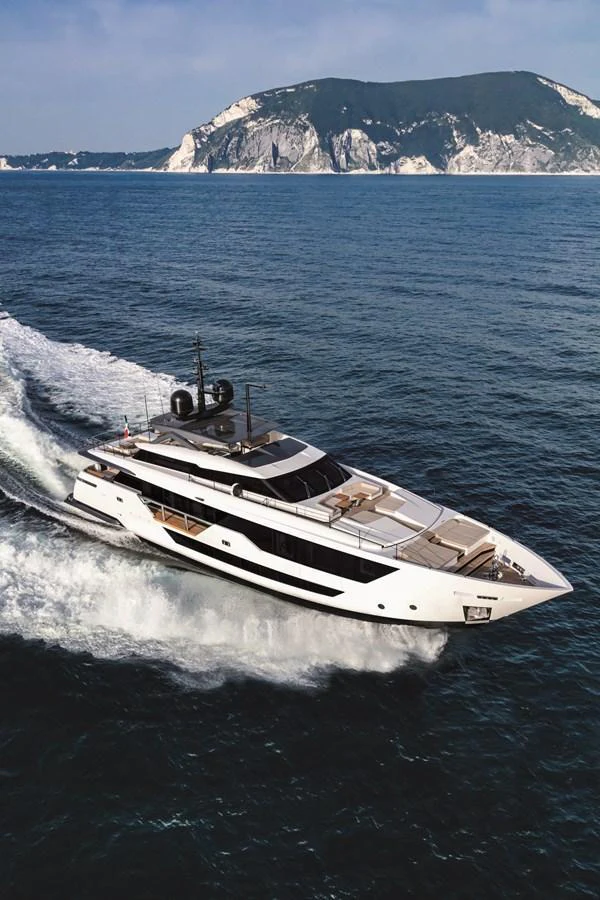A sleek yacht cruises through the open sea with a picturesque mountainous backdrop. aboard CUSTOM LINE SAETTA 128/02 Yacht for Sale