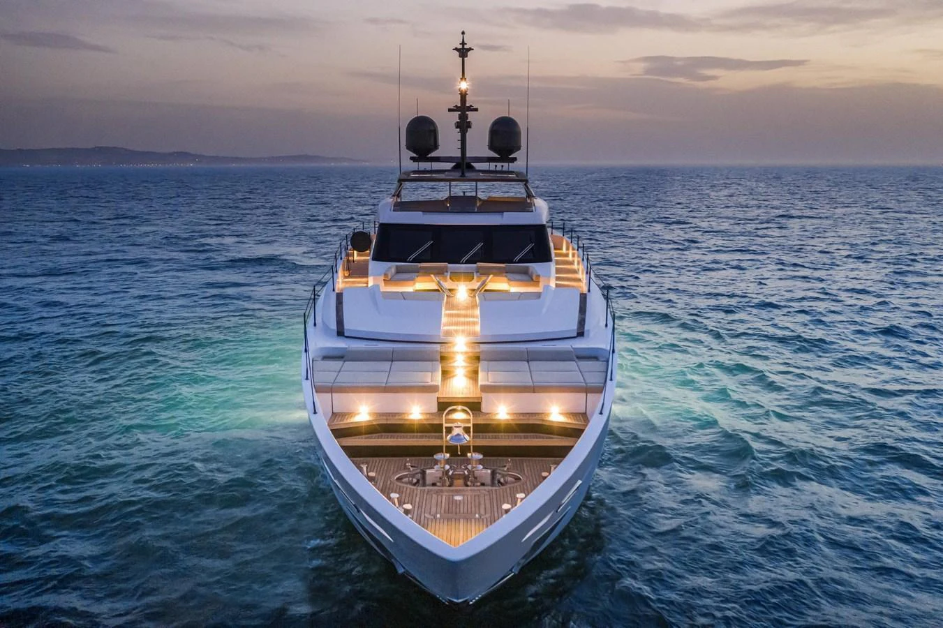 A sleek yacht is beautifully illuminated against the backdrop of a serene ocean at dusk. aboard CUSTOM LINE SAETTA 128/02 Yacht for Sale