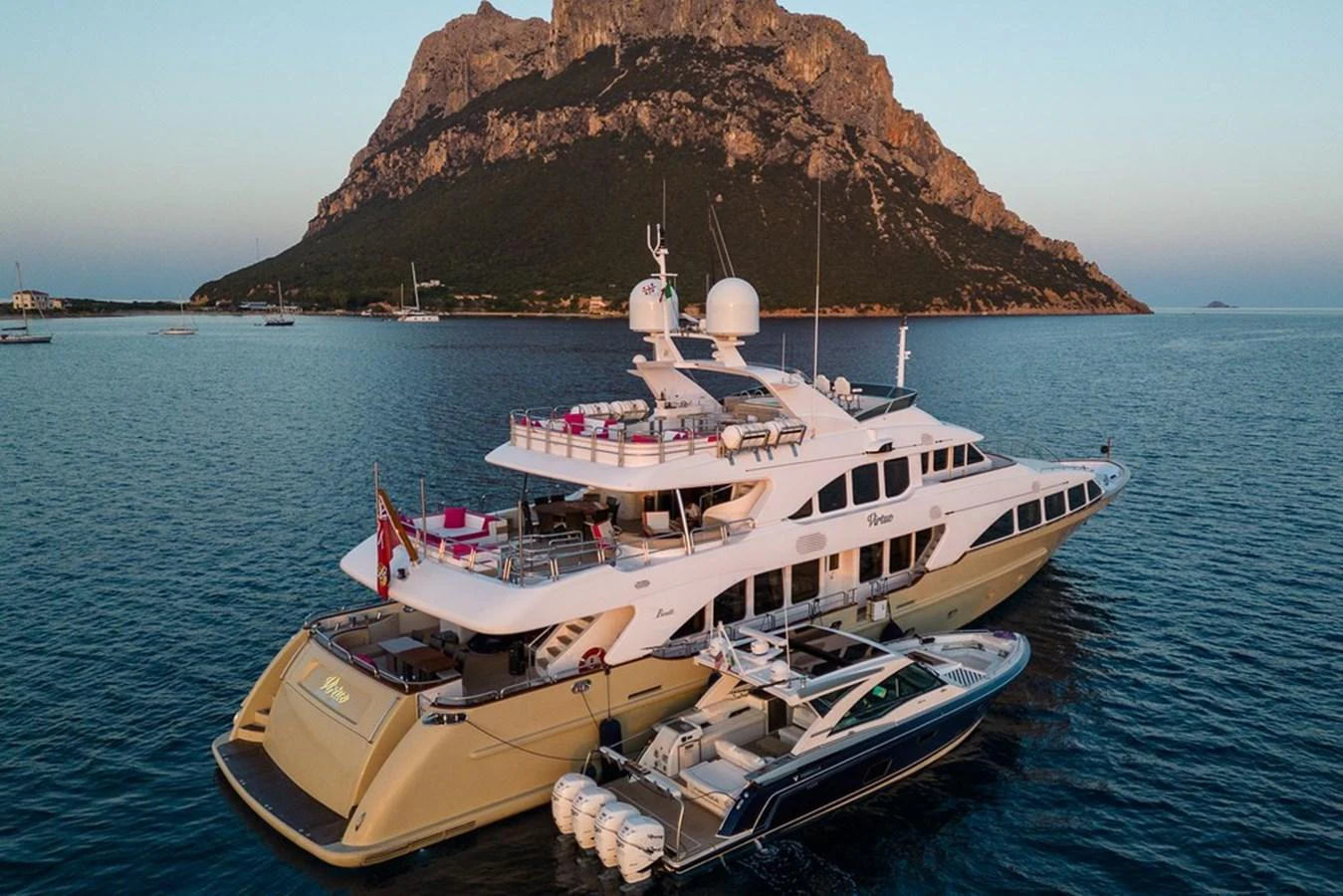 A luxurious yacht anchored near a scenic island, accompanied by a sleek tender. aboard VIRTUE Yacht for Sale