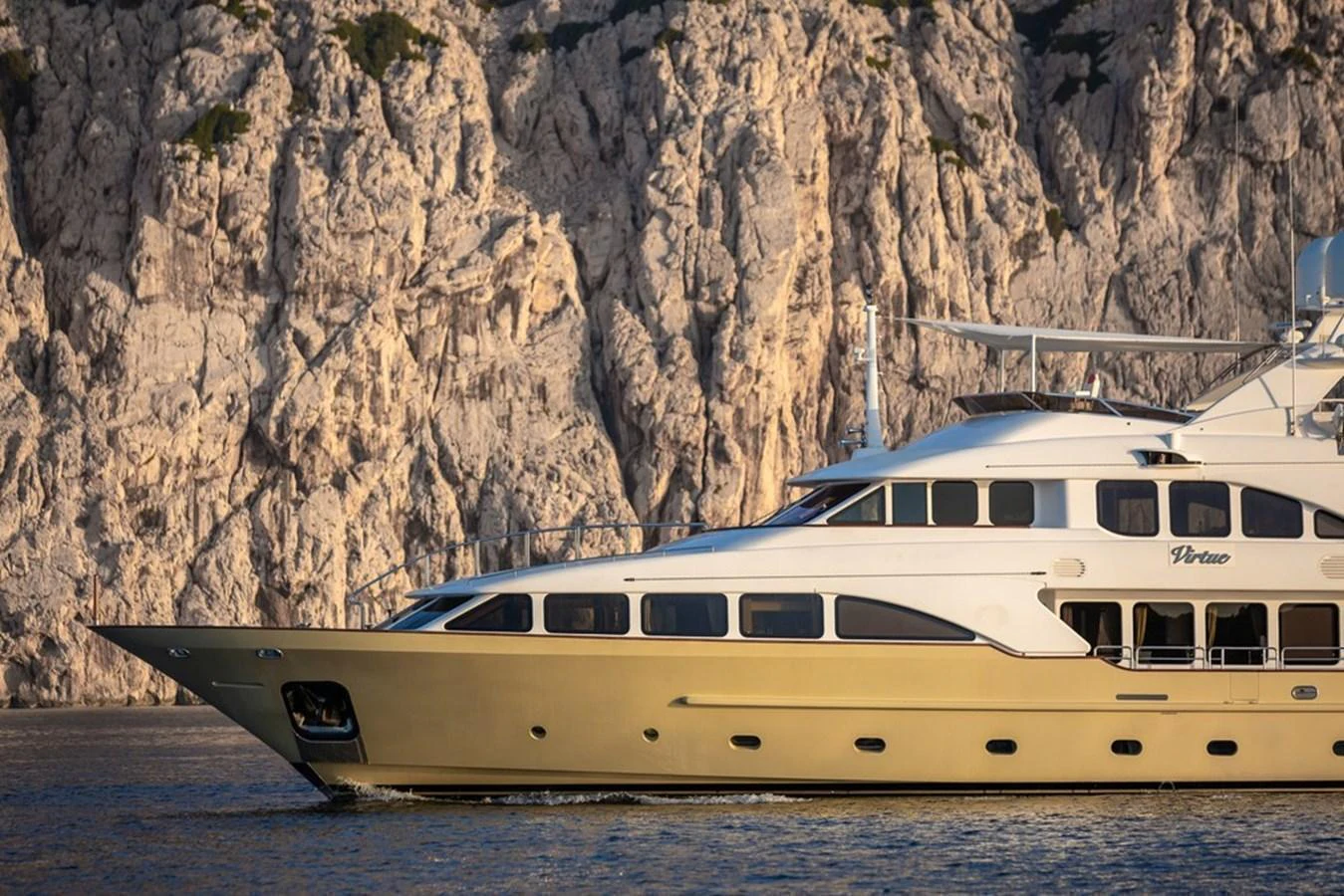 A luxurious yacht cruises along a rocky coastline, showcasing its elegant design and spacious decks. aboard VIRTUE Yacht for Sale
