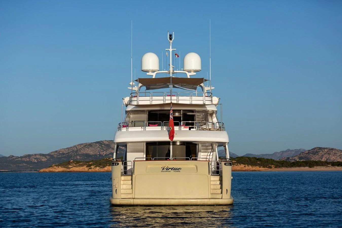 The yacht is anchored in calm waters with a scenic backdrop of mountains and clear skies. aboard VIRTUE Yacht for Sale