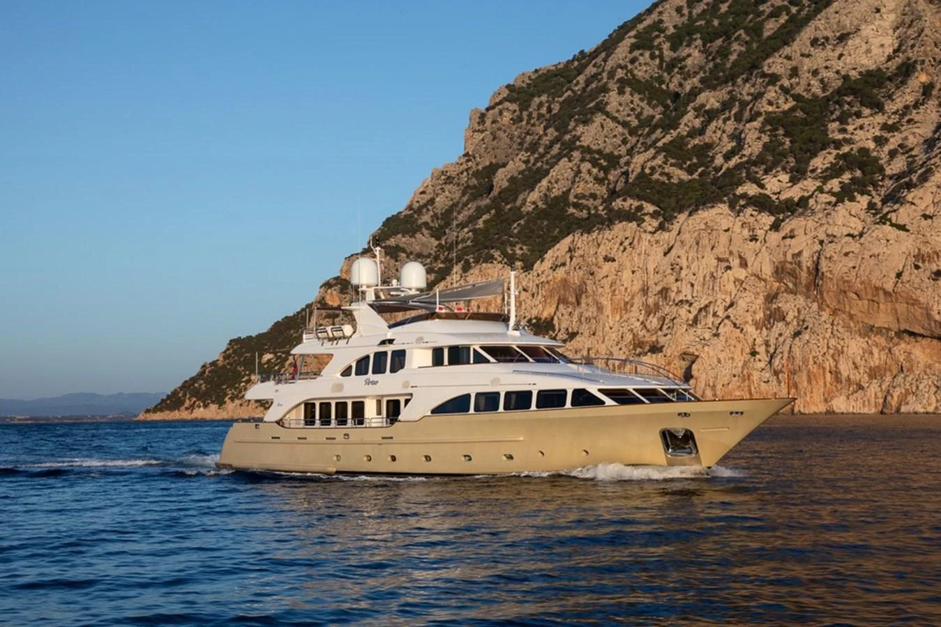 A luxurious yacht cruises along a scenic coastline with rugged cliffs in the background. aboard VIRTUE Yacht for Sale