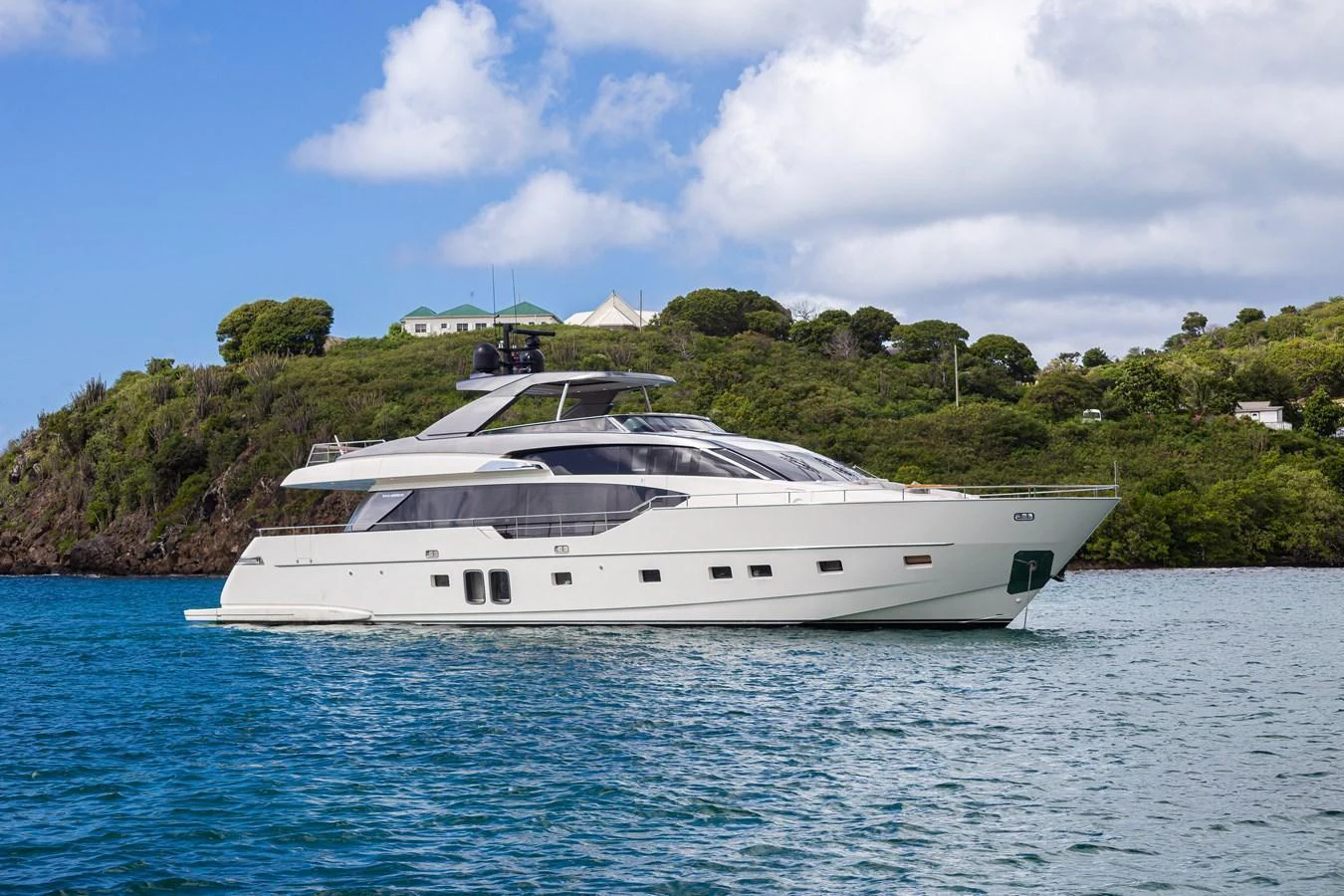 A sleek and modern yacht cruising in tranquil blue waters with a lush green island in the background. aboard AKULA Yacht for Sale