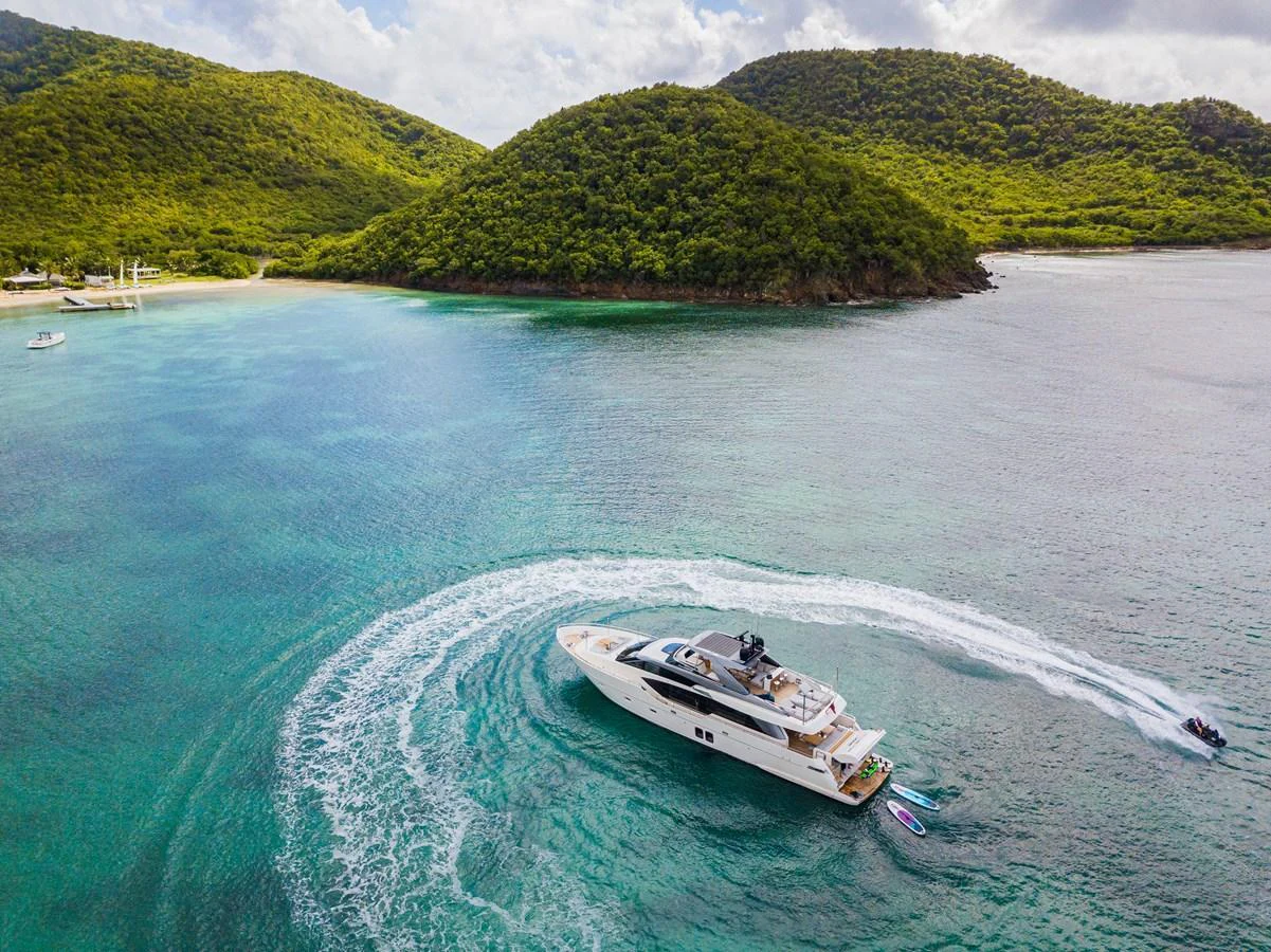 A sleek yacht cruises through crystal-clear waters near a lush, green island. aboard AKULA Yacht for Sale
