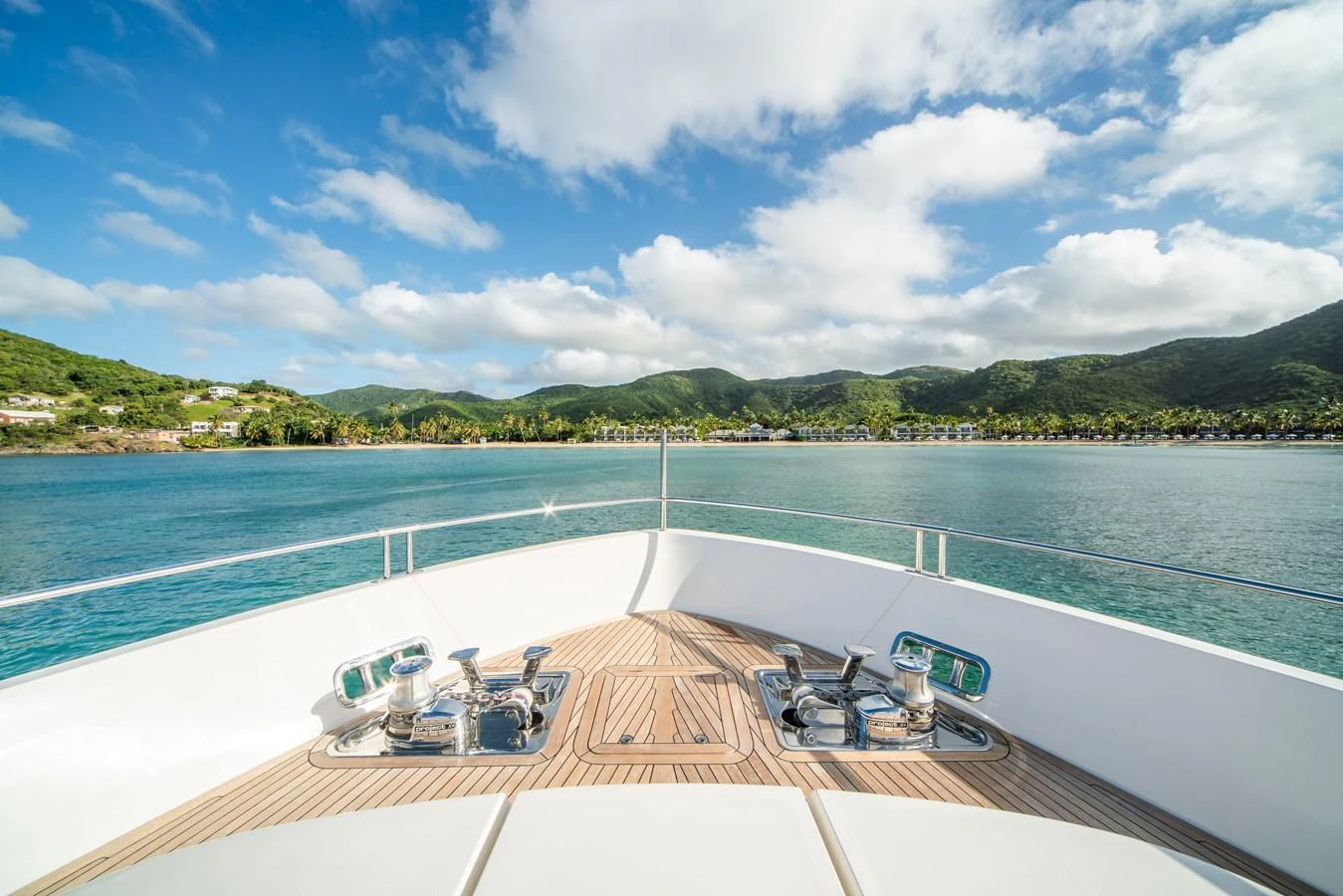 The bow of the yacht offers a serene view of the surrounding waters and lush green hills under a bright blue sky. aboard AKULA Yacht for Sale