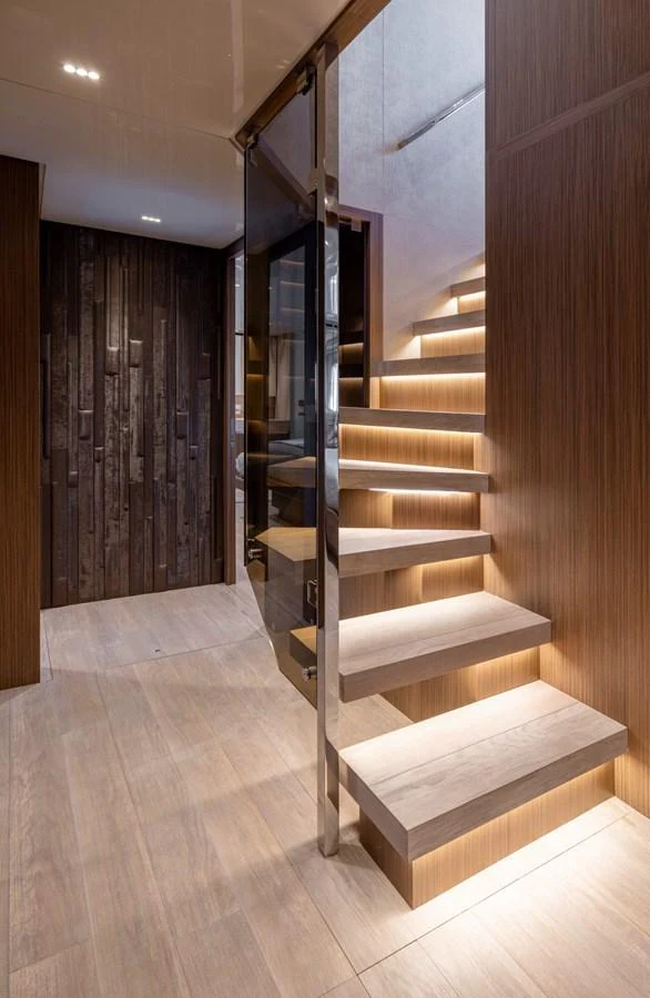 A modern staircase with sleek wooden steps and ambient lighting leads to the upper deck. aboard LADY LU' Yacht for Sale