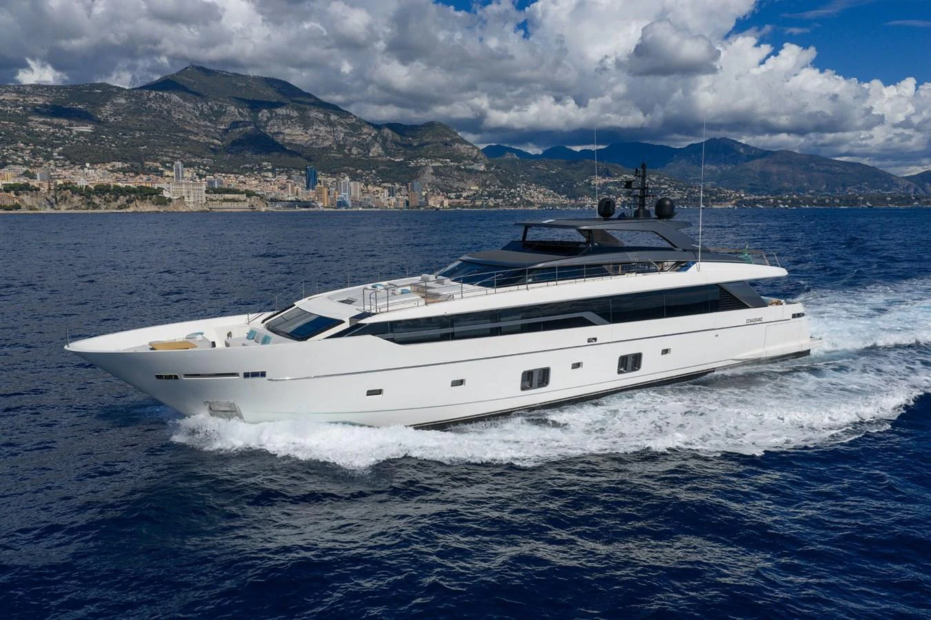 A sleek and modern yacht cruises through the open water with a stunning coastal backdrop. aboard LADY LU' Yacht for Sale
