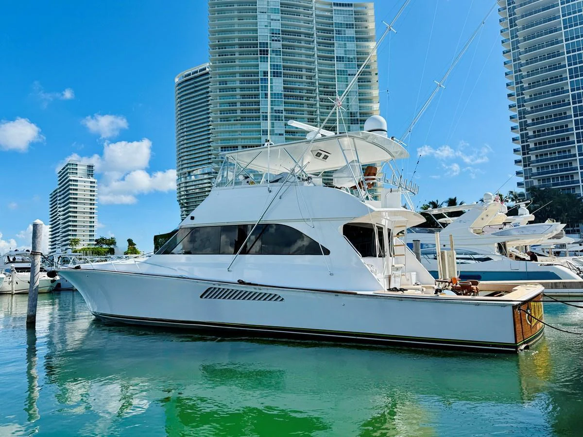 A sleek yacht is docked in a marina with a backdrop of modern high-rise buildings. aboard KICKBACK Yacht for Sale