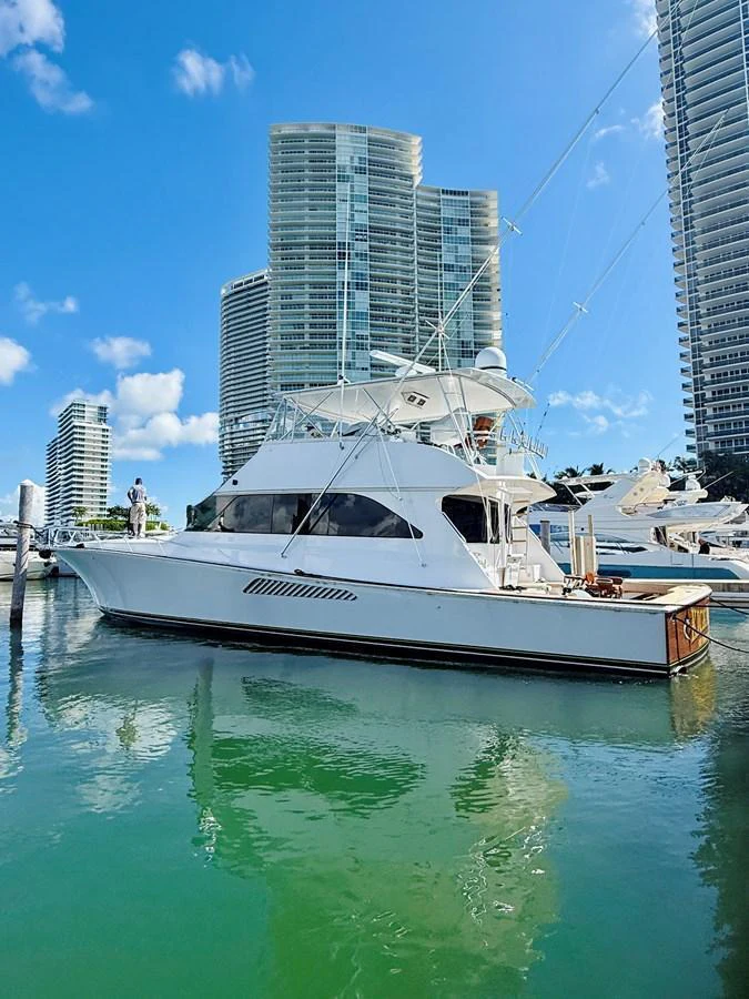 A sleek white yacht is docked in a marina with modern high-rise buildings in the background. aboard KICKBACK Yacht for Sale