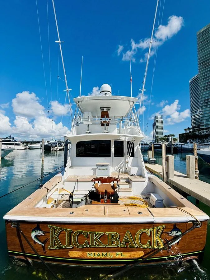 The stern of the yacht is docked at a marina, showcasing its name and fishing equipment. aboard KICKBACK Yacht for Sale