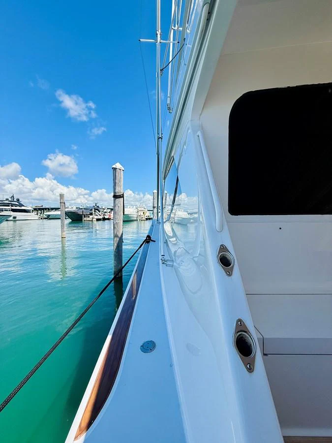 The yacht is docked at a marina, showcasing its sleek side profile against a backdrop of clear blue skies and calm waters. aboard KICKBACK Yacht for Sale