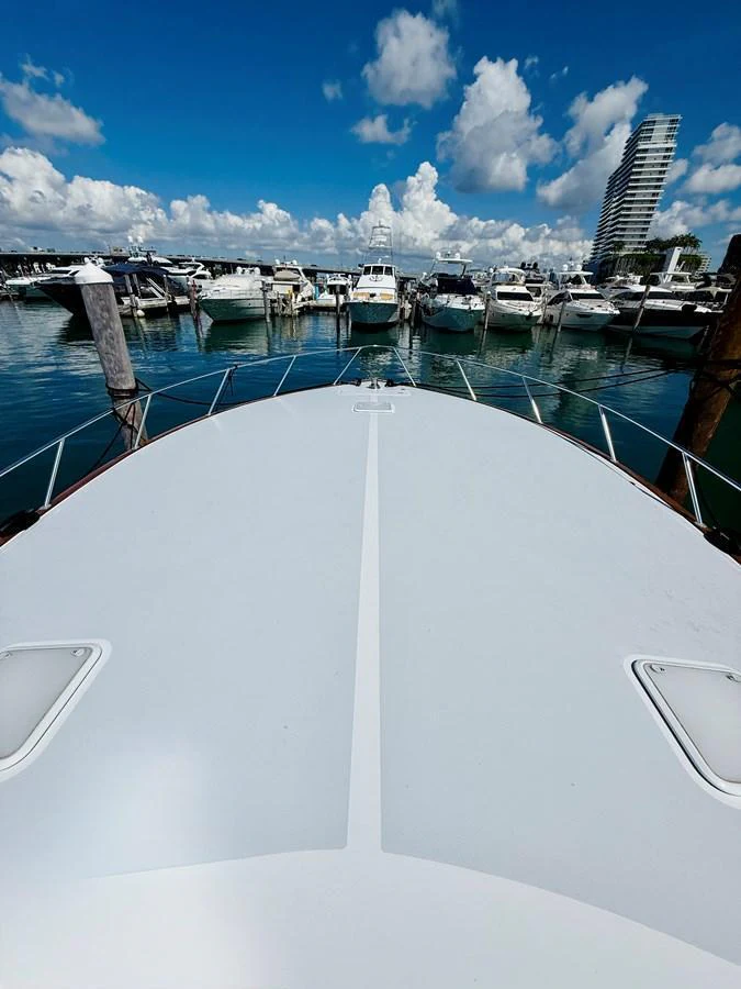 The yacht is docked in a bustling marina under a bright blue sky with scattered clouds. aboard KICKBACK Yacht for Sale