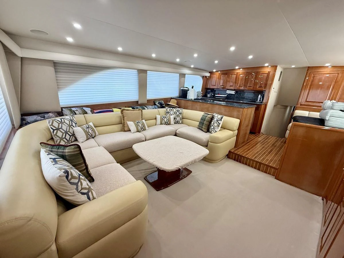 The spacious salon features a plush, cream-colored sectional sofa and a modern galley with rich wood cabinetry. aboard KICKBACK Yacht for Sale