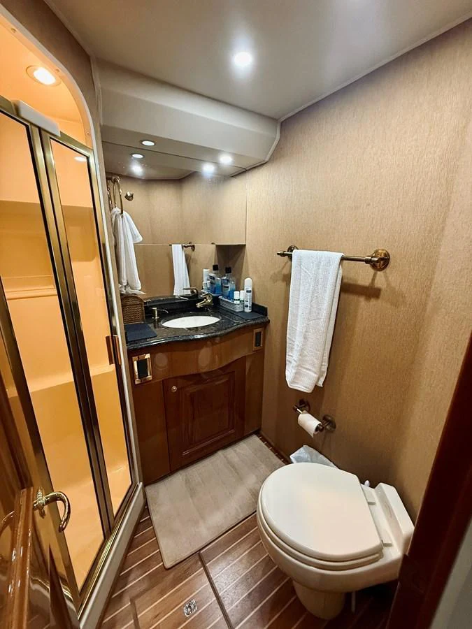 A well-appointed yacht bathroom featuring a sink, toilet, and shower with elegant wood finishes. aboard KICKBACK Yacht for Sale