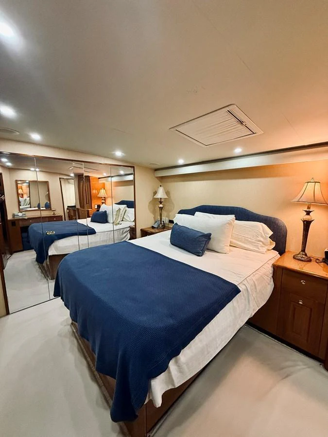 A cozy stateroom featuring a comfortable bed with blue bedding and elegant wooden cabinetry. aboard KICKBACK Yacht for Sale