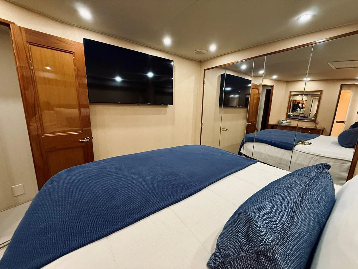 A cozy stateroom featuring a large bed with blue bedding, a wall-mounted TV, and mirrored closet doors. aboard KICKBACK Yacht for Sale