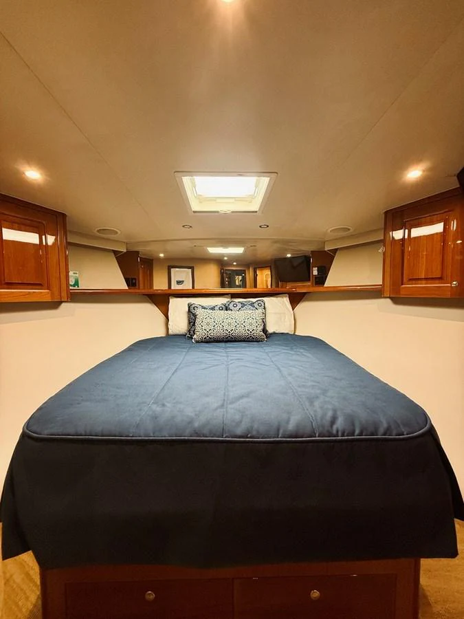 A cozy stateroom featuring a comfortable bed with elegant bedding and warm wooden cabinetry. aboard KICKBACK Yacht for Sale