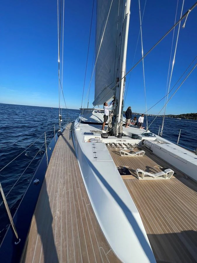 The sleek deck of a sailing yacht glides smoothly over calm waters under a clear blue sky. aboard MUMU Yacht for Sale