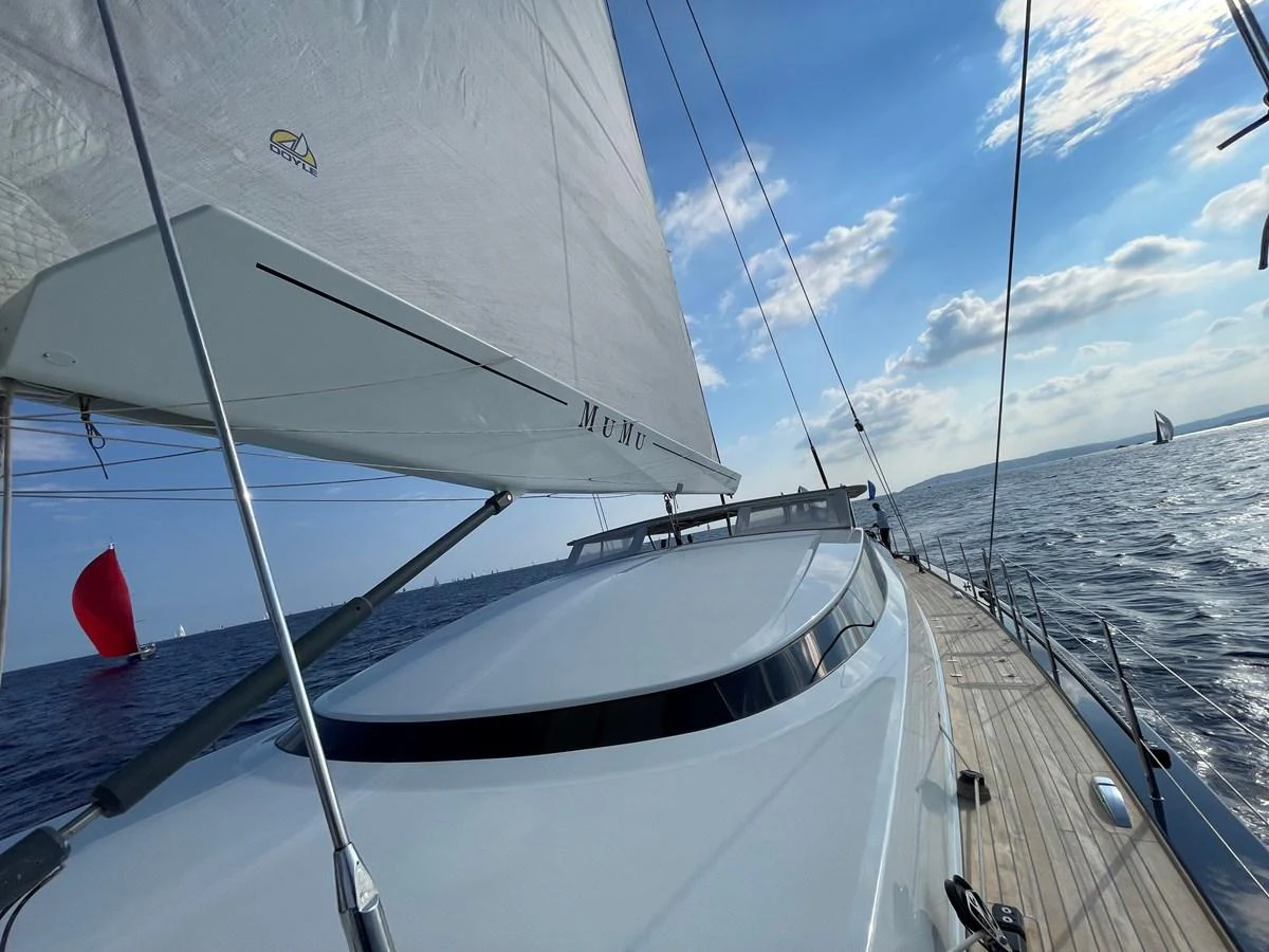 The sleek deck of a sailing yacht glides smoothly over the water under a clear blue sky. aboard MUMU Yacht for Sale