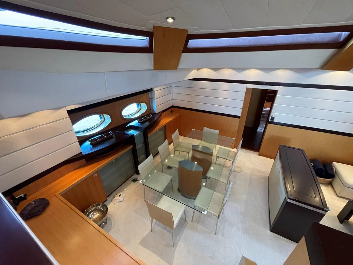The yacht's dining area features a modern glass table with seating for six, surrounded by elegant wood and white paneling. aboard MUMU Yacht for Sale