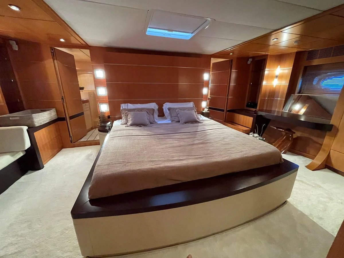 The master stateroom features a spacious bed with elegant wood paneling and ample lighting. aboard MUMU Yacht for Sale