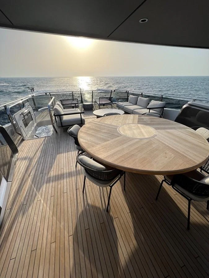 The aft deck features a stylish outdoor dining area with a round wooden table and comfortable seating, perfect for enjoying meals with a view of the sea. aboard SEMIA Yacht for Sale