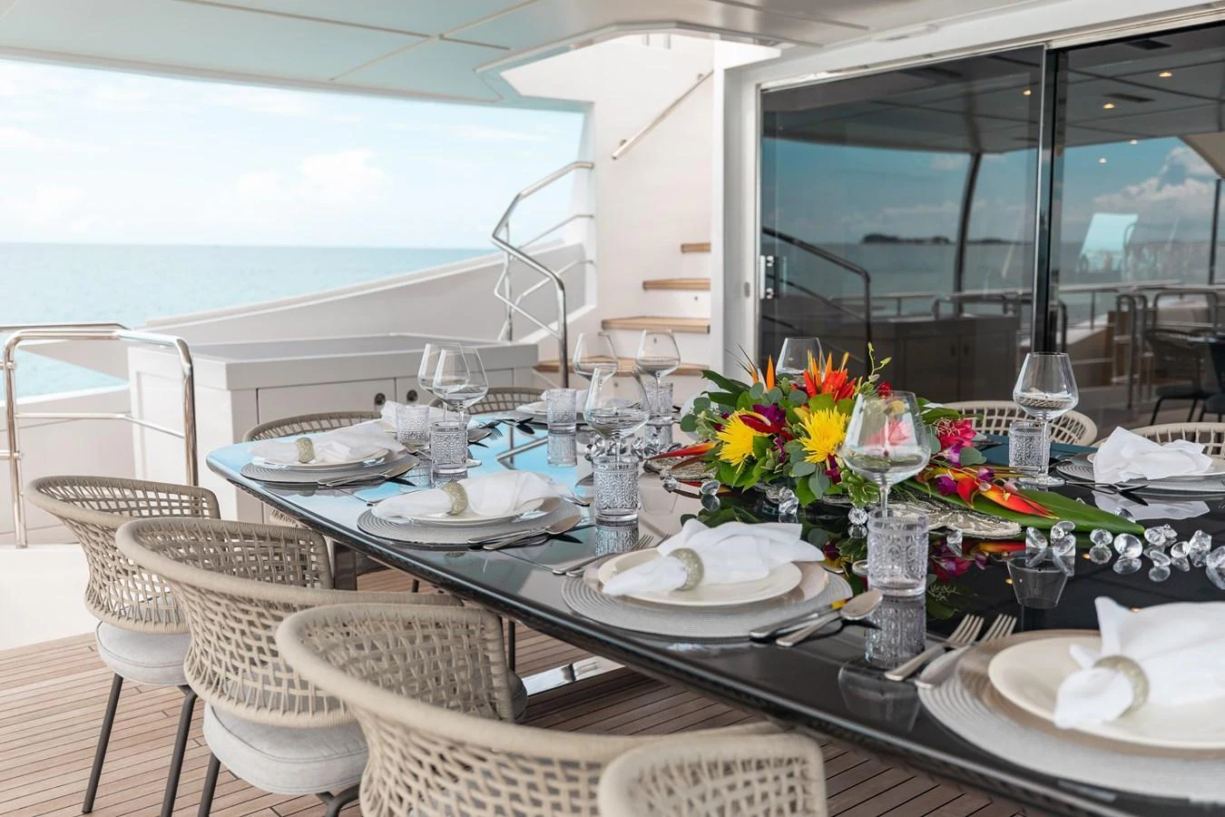 The aft deck features an elegant dining area with a beautifully set table, perfect for alfresco meals with a view of the sea. aboard EMINA Yacht for Sale