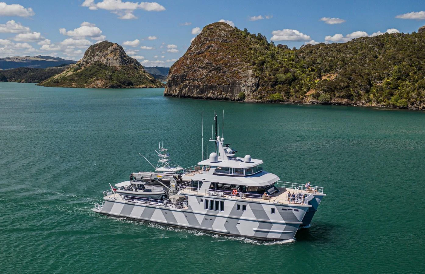 A stunning yacht cruises through serene green waters with picturesque rocky hills in the background. aboard THE BEAST Yacht for Sale