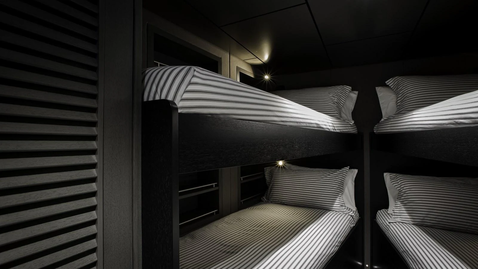 The cozy bunk room features neatly arranged striped bedding and a modern, minimalist design. aboard THE BEAST Yacht for Sale