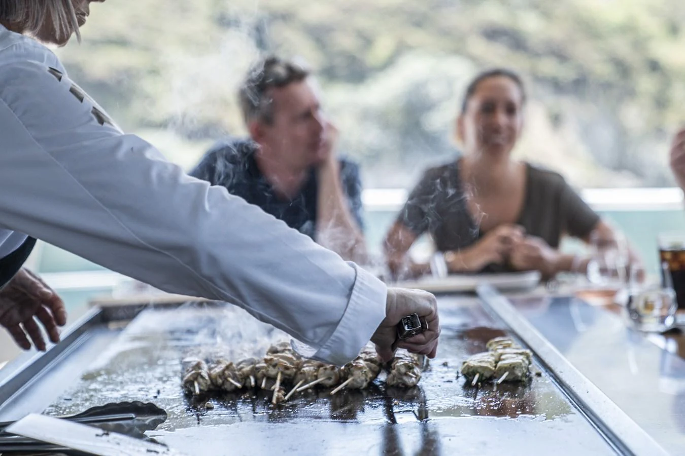 An outdoor dining area with a chef preparing skewers on a grill, surrounded by guests. aboard THE BEAST Yacht for Sale