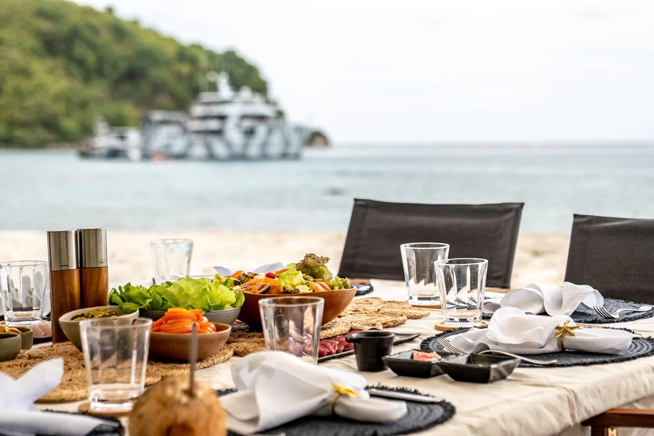 A beautifully set dining table on the beach with a yacht in the background. aboard THE BEAST Yacht for Sale