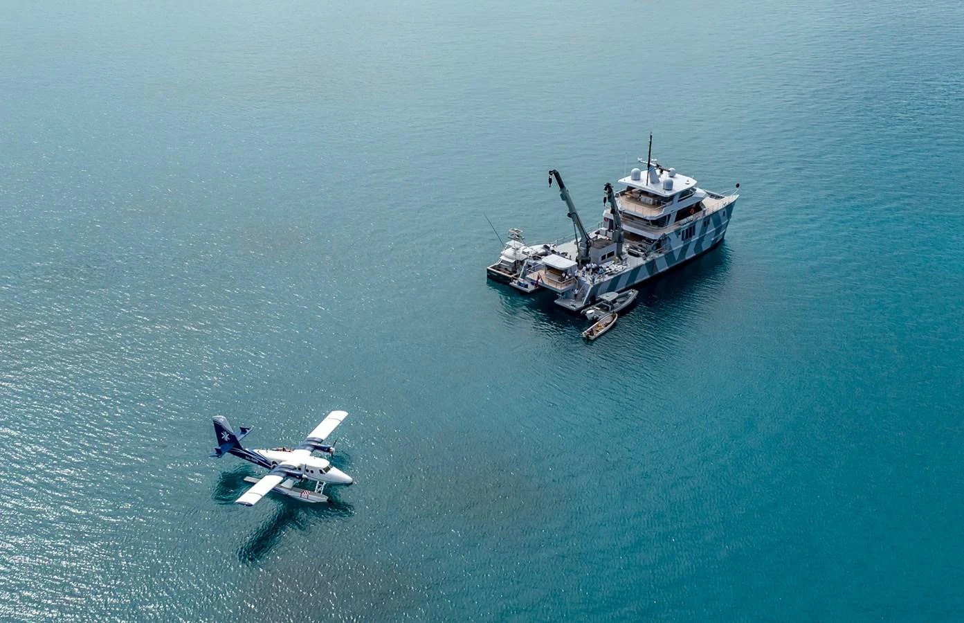 A yacht anchored in calm waters with a seaplane nearby, showcasing a unique camouflage design. aboard THE BEAST Yacht for Sale