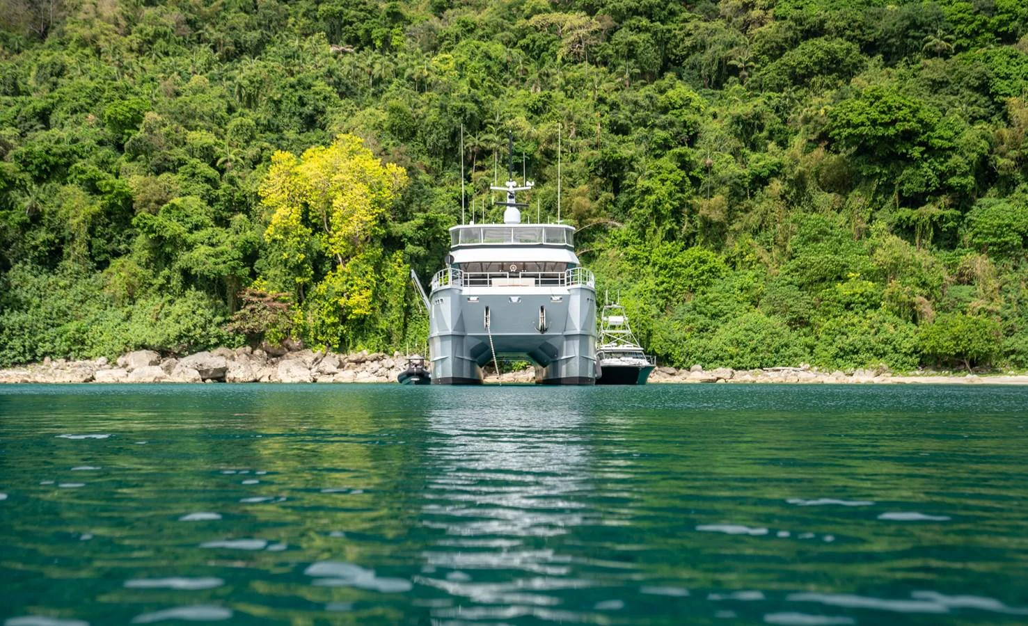 A yacht is anchored in a serene, lush green bay, viewed head-on from the water. aboard THE BEAST Yacht for Sale