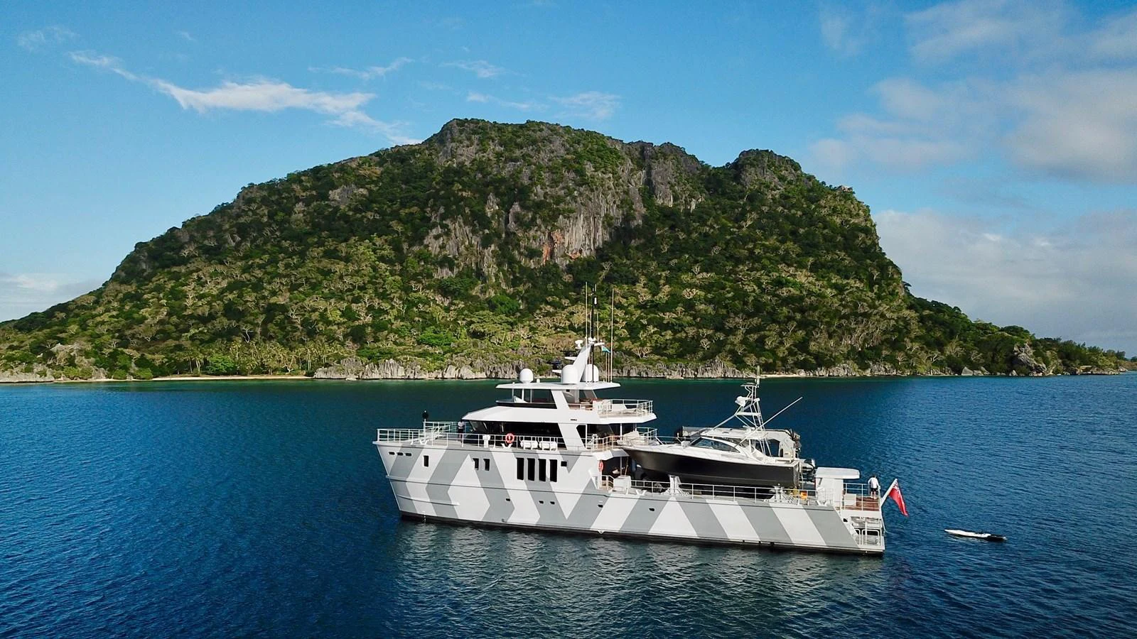 A sleek yacht is anchored in a serene bay with a lush, green island in the background. aboard THE BEAST Yacht for Sale