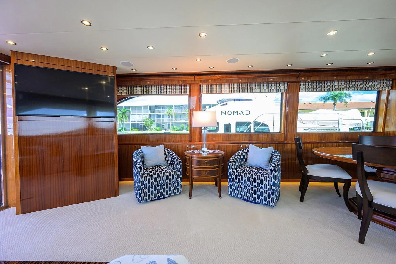 The yacht's interior features a cozy seating area with two patterned armchairs and a dining table, illuminated by natural light through large windows. aboard SAPPHIRE Yacht for Sale