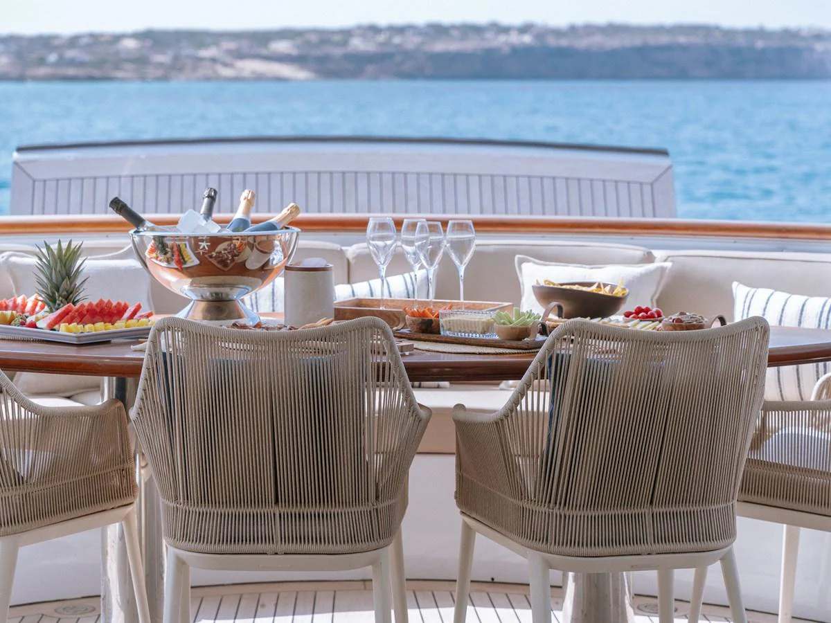 The aft deck features an elegant dining setup with a scenic ocean view. aboard FRIENDSHIP Yacht for Sale