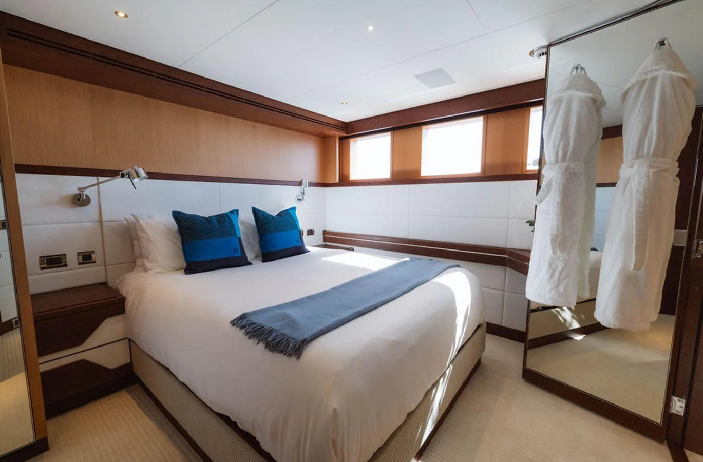 The stateroom features a luxurious bed with plush pillows and a cozy blanket, complemented by elegant wood paneling and ample natural light. aboard GRAYCLIFFS Yacht for Sale