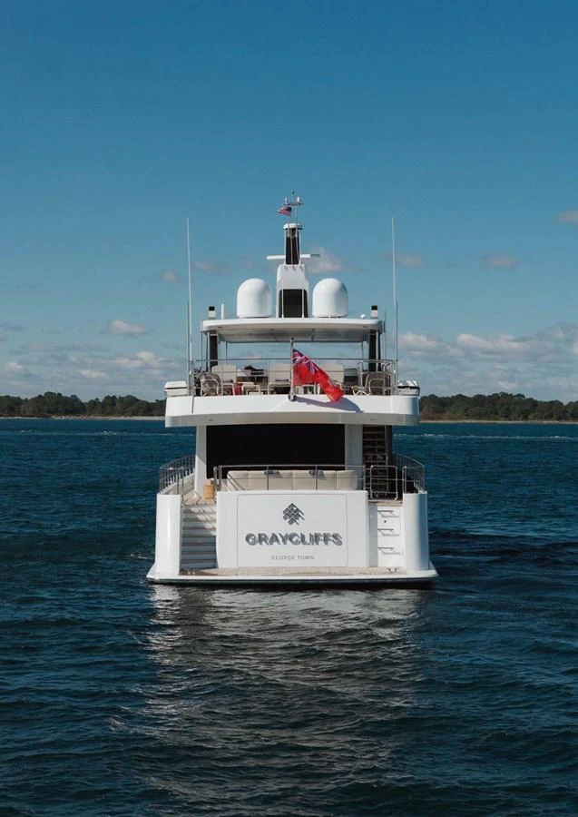 A luxurious yacht is seen from the rear, cruising on calm waters under a clear blue sky. aboard GRAYCLIFFS Yacht for Sale