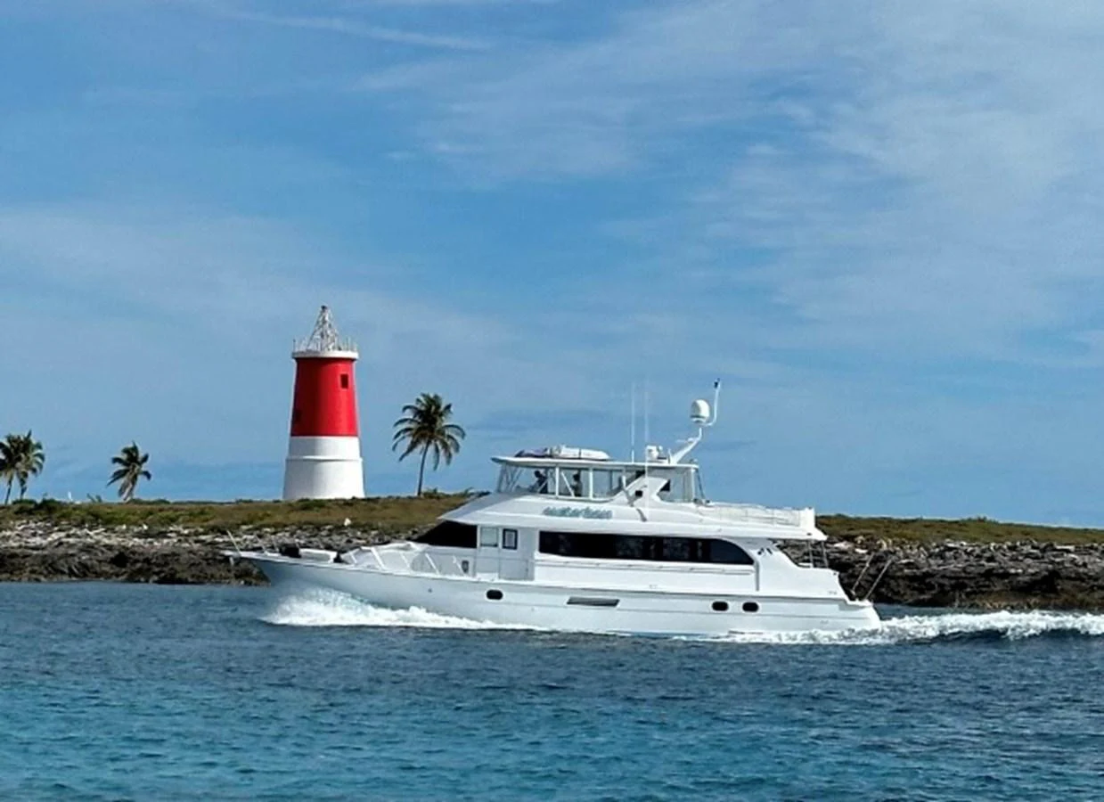 A sleek white yacht cruises past a picturesque lighthouse and palm trees on a clear day. aboard WATER BORN Yacht for Sale