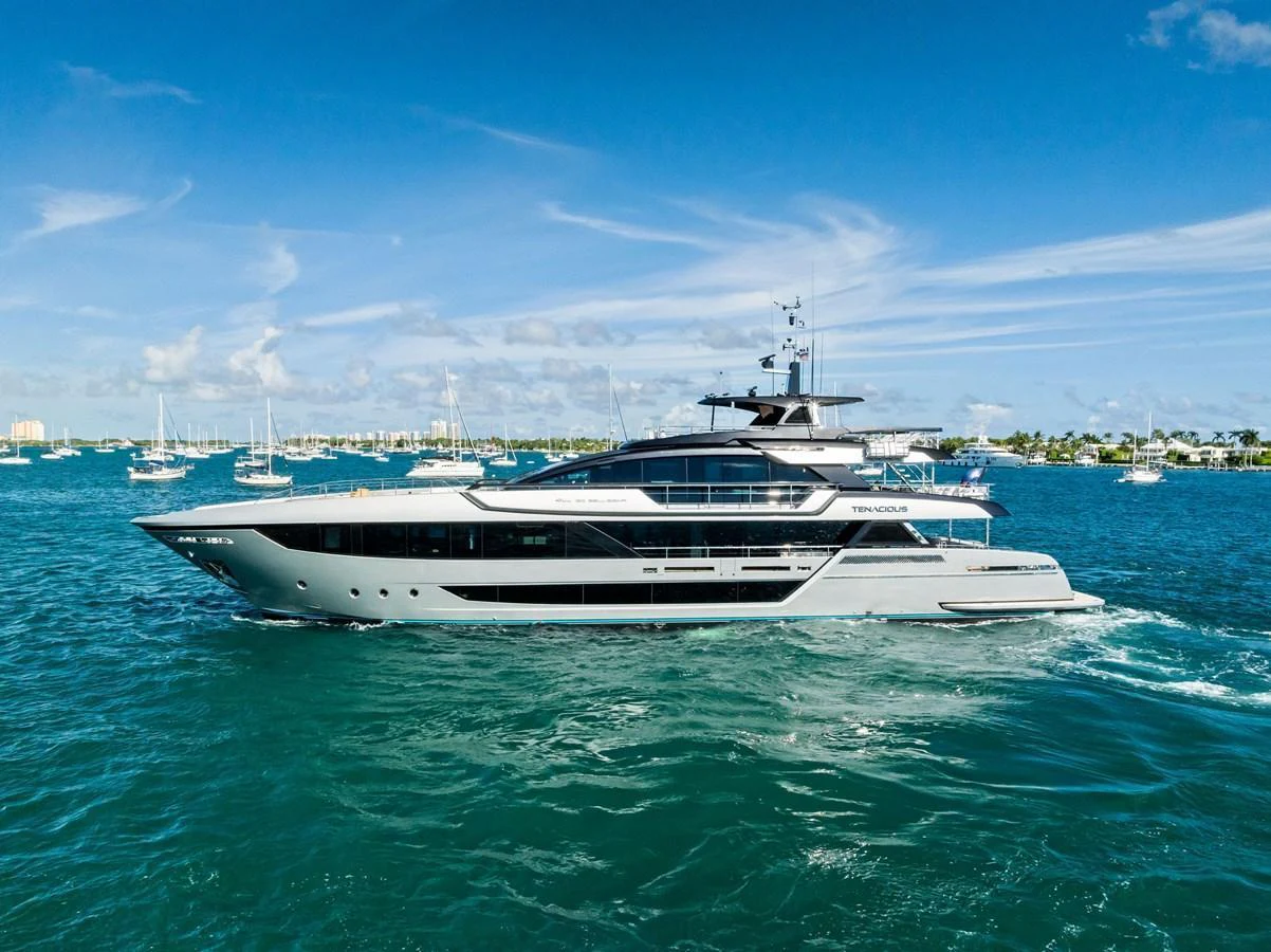 A sleek and modern yacht cruises through vibrant blue waters under a clear sky. aboard TENACIOUS Yacht for Sale