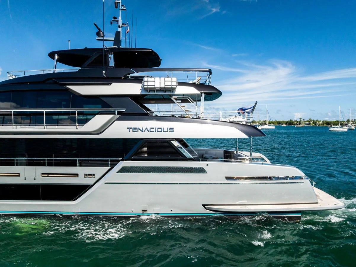 A sleek and modern yacht glides through the water under a clear blue sky. aboard TENACIOUS Yacht for Sale
