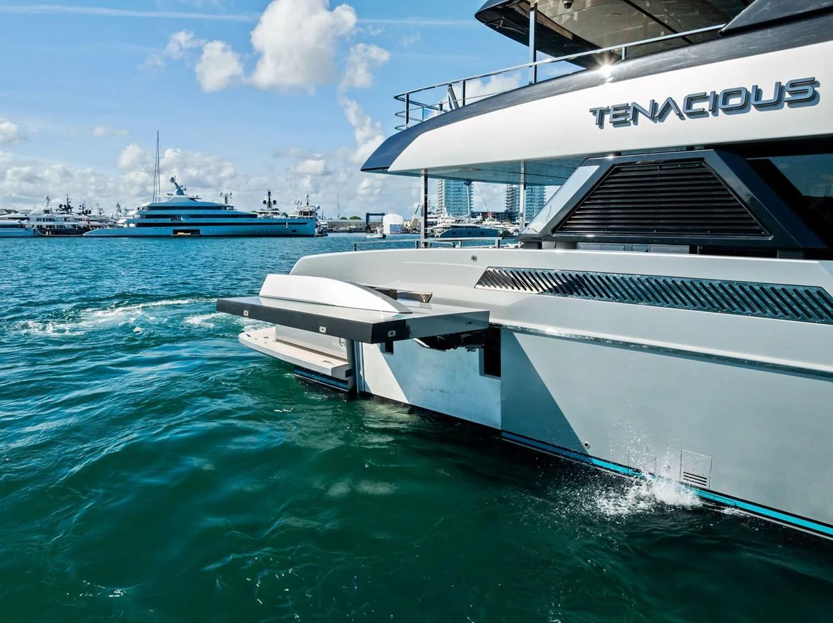 The yacht is seen from the side, showcasing its sleek design and a fold-out platform over the water. aboard TENACIOUS Yacht for Sale