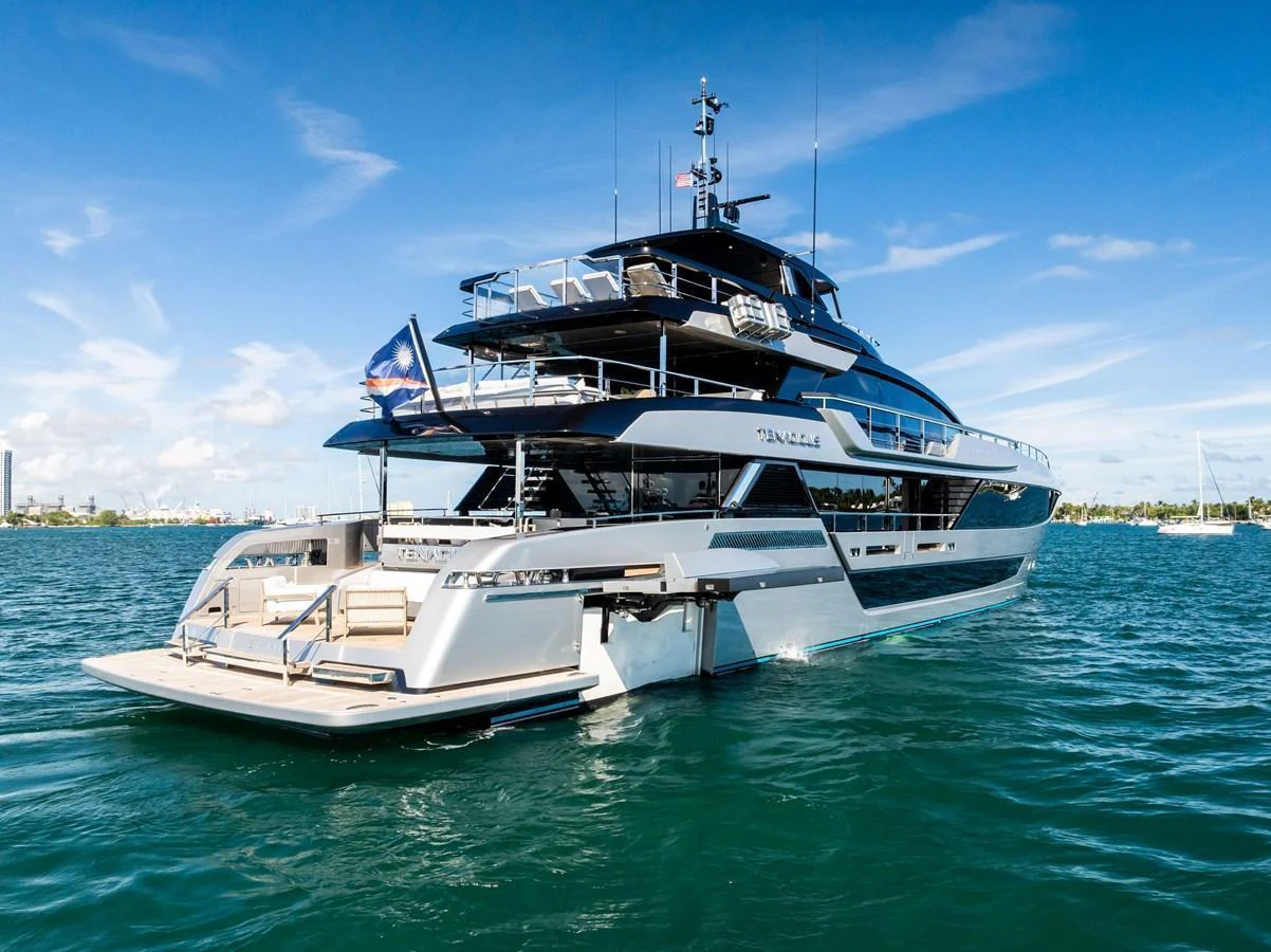 A sleek and modern yacht with multiple decks is cruising on calm waters under a clear blue sky. aboard TENACIOUS Yacht for Sale