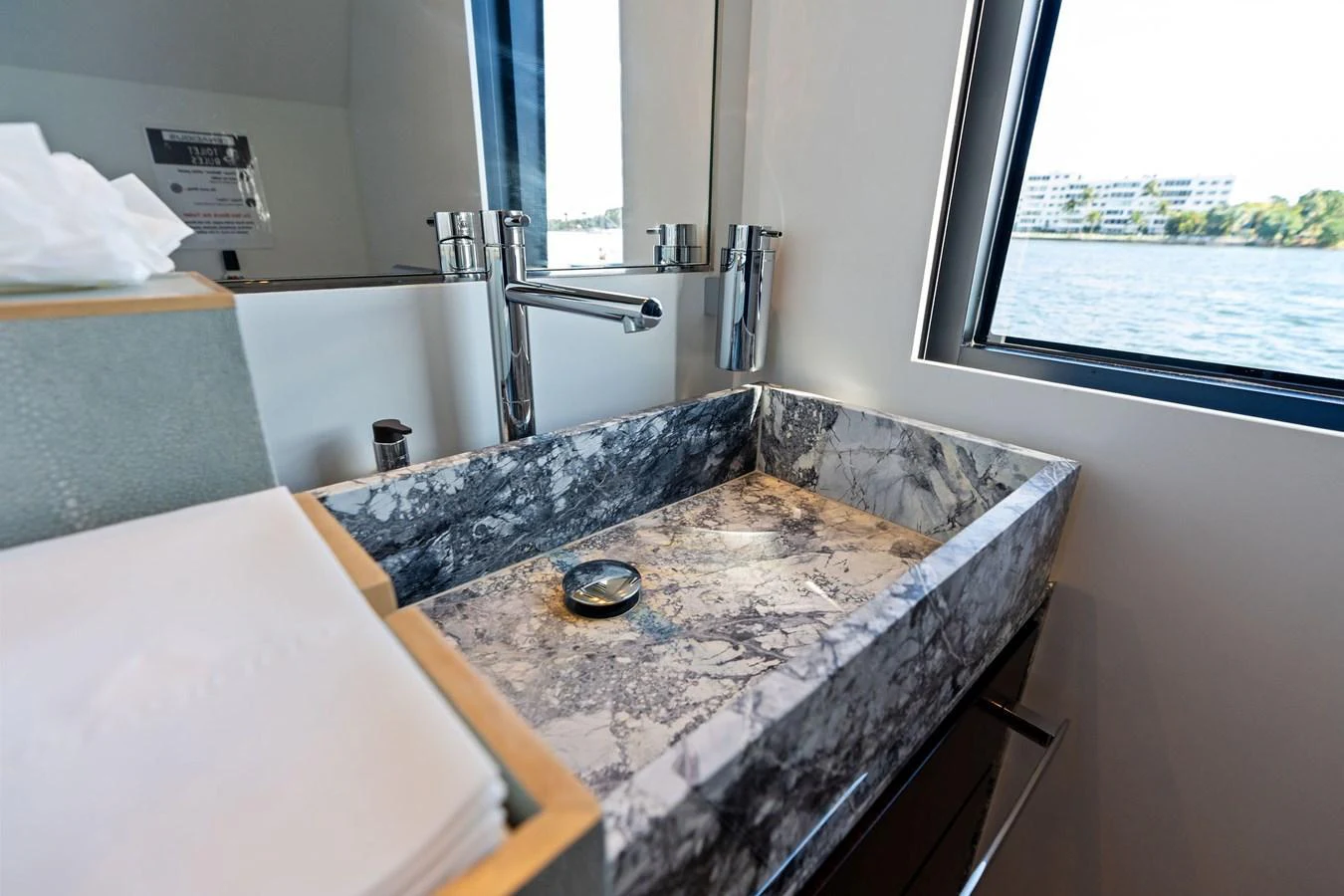 A luxurious yacht bathroom featuring a sleek marble sink and a view of the water through the window. aboard TENACIOUS Yacht for Sale