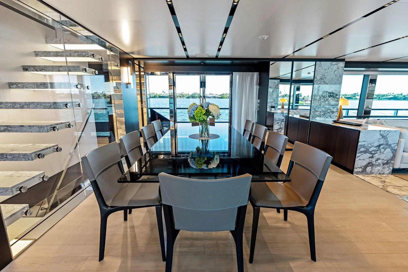 The yacht's dining area features a sleek, modern design with a large table and ample seating, complemented by panoramic windows offering stunning views. aboard TENACIOUS Yacht for Sale