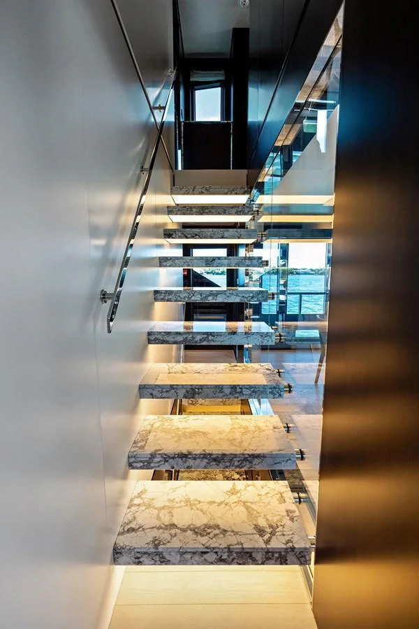 A luxurious marble staircase with glass railings leads to the upper deck, showcasing modern design and elegance. aboard TENACIOUS Yacht for Sale