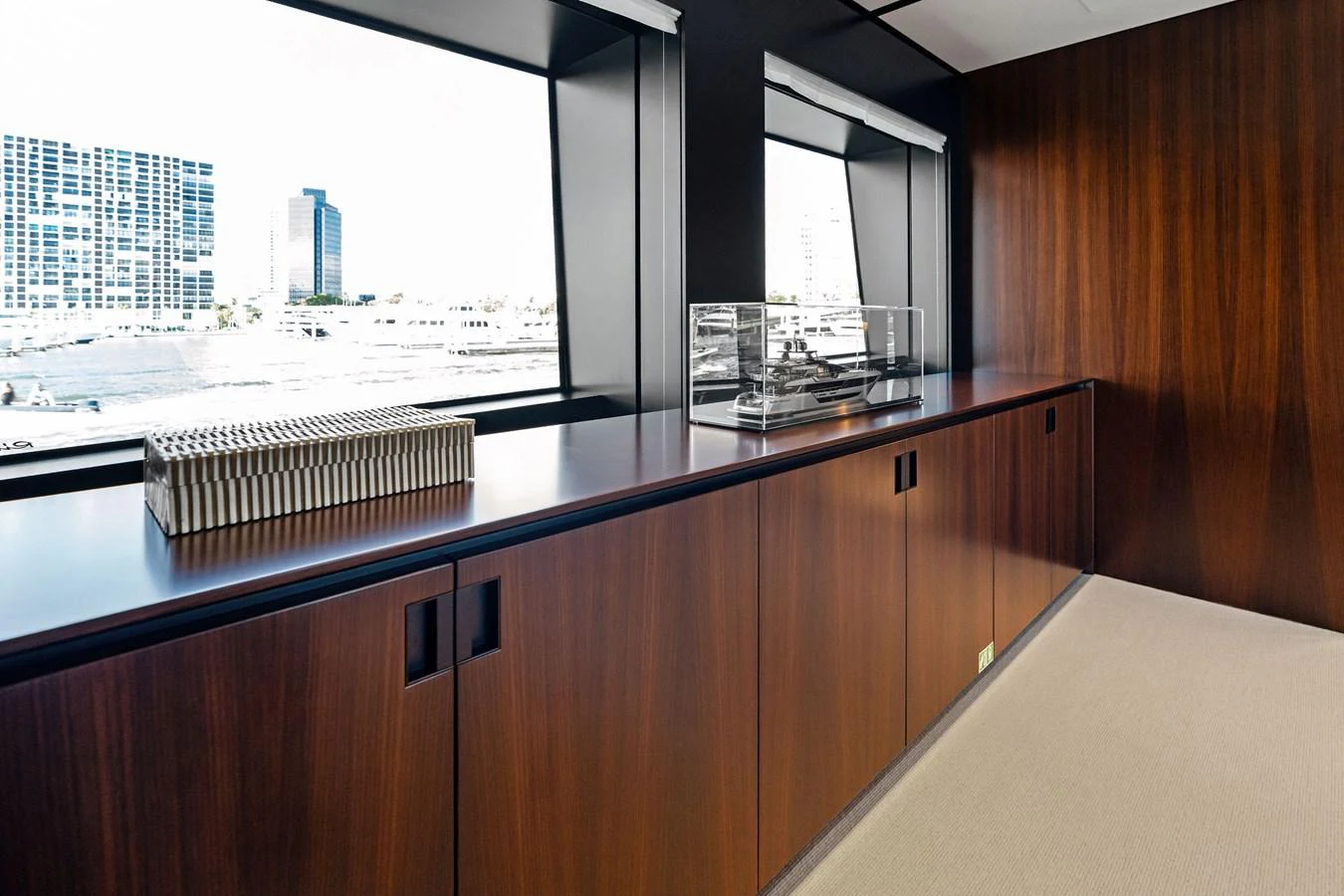 This image showcases a sleek, modern interior space with rich wood paneling and large windows offering a view of the cityscape. aboard TENACIOUS Yacht for Sale