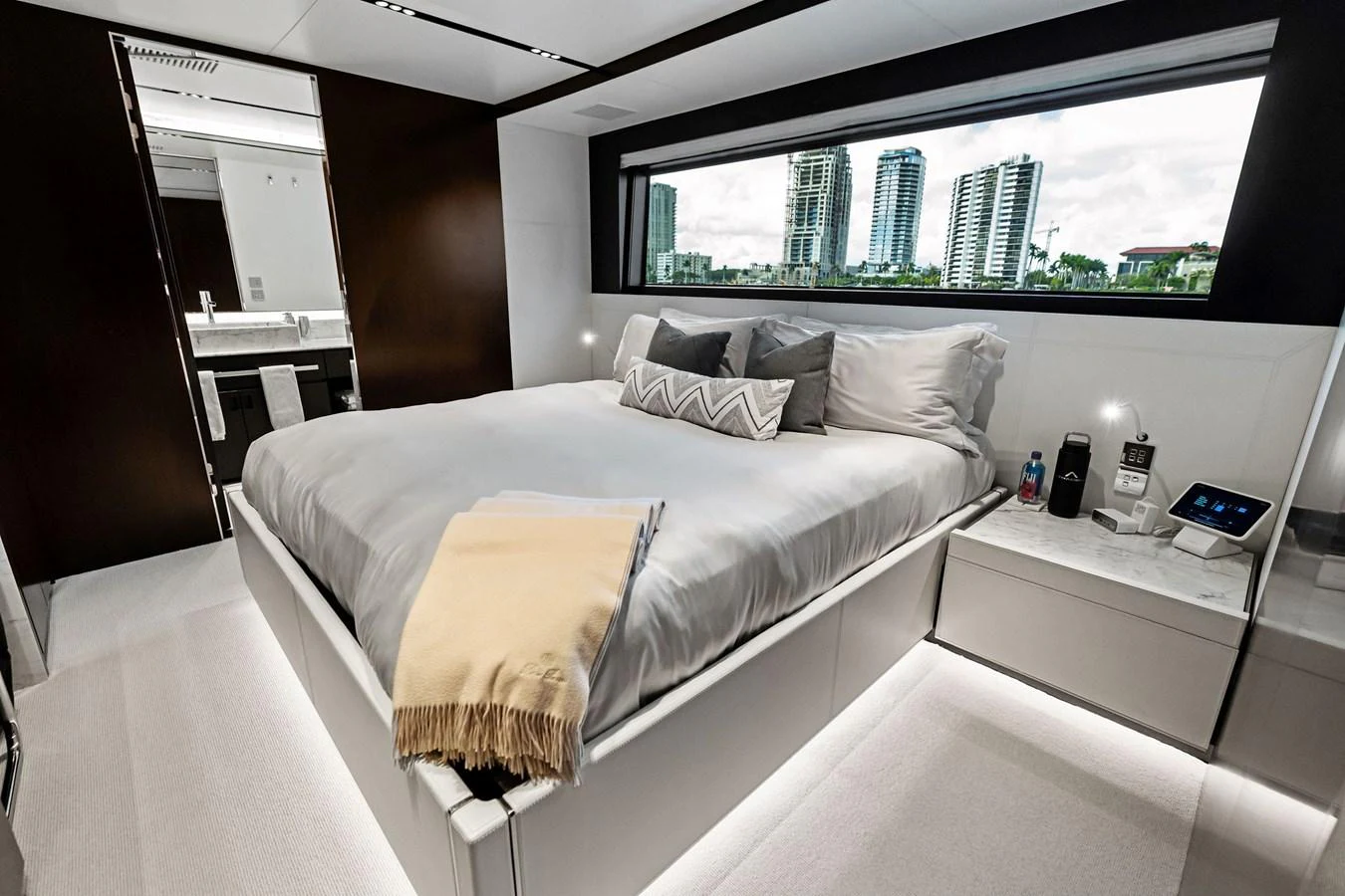 The stateroom features a luxurious bed with a large window offering a stunning view of the city skyline. aboard TENACIOUS Yacht for Sale